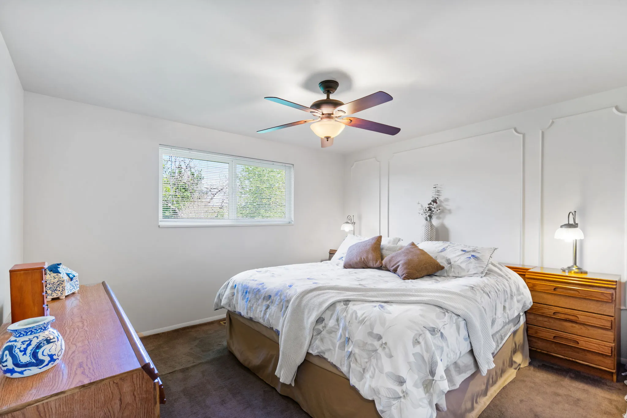 Bedroom featuring a ceiling fan with integrated lighting, a window, wall paneling, and neutral-toned carpeting