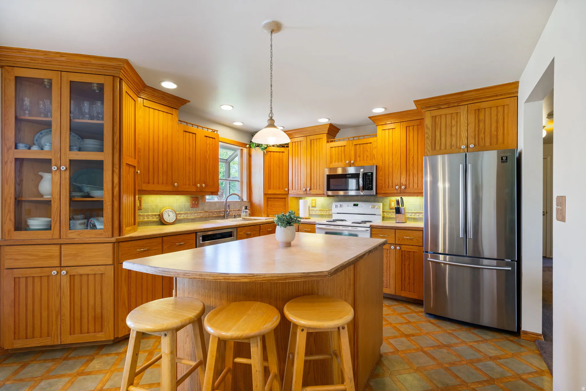 Kitchen featuring a central island with seating, ample wood cabinetry, glass-front upper cabinets, stainless steel appliances, and wood-finish flooring