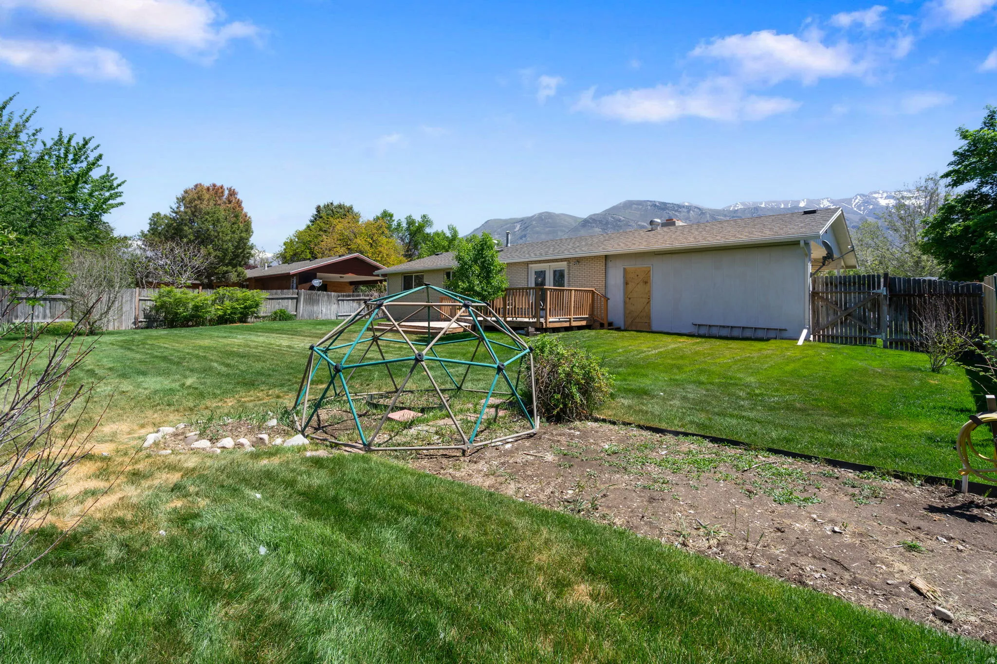 Expansive backyard featuring a lush lawn, mature perimeter trees, and a wooden deck
