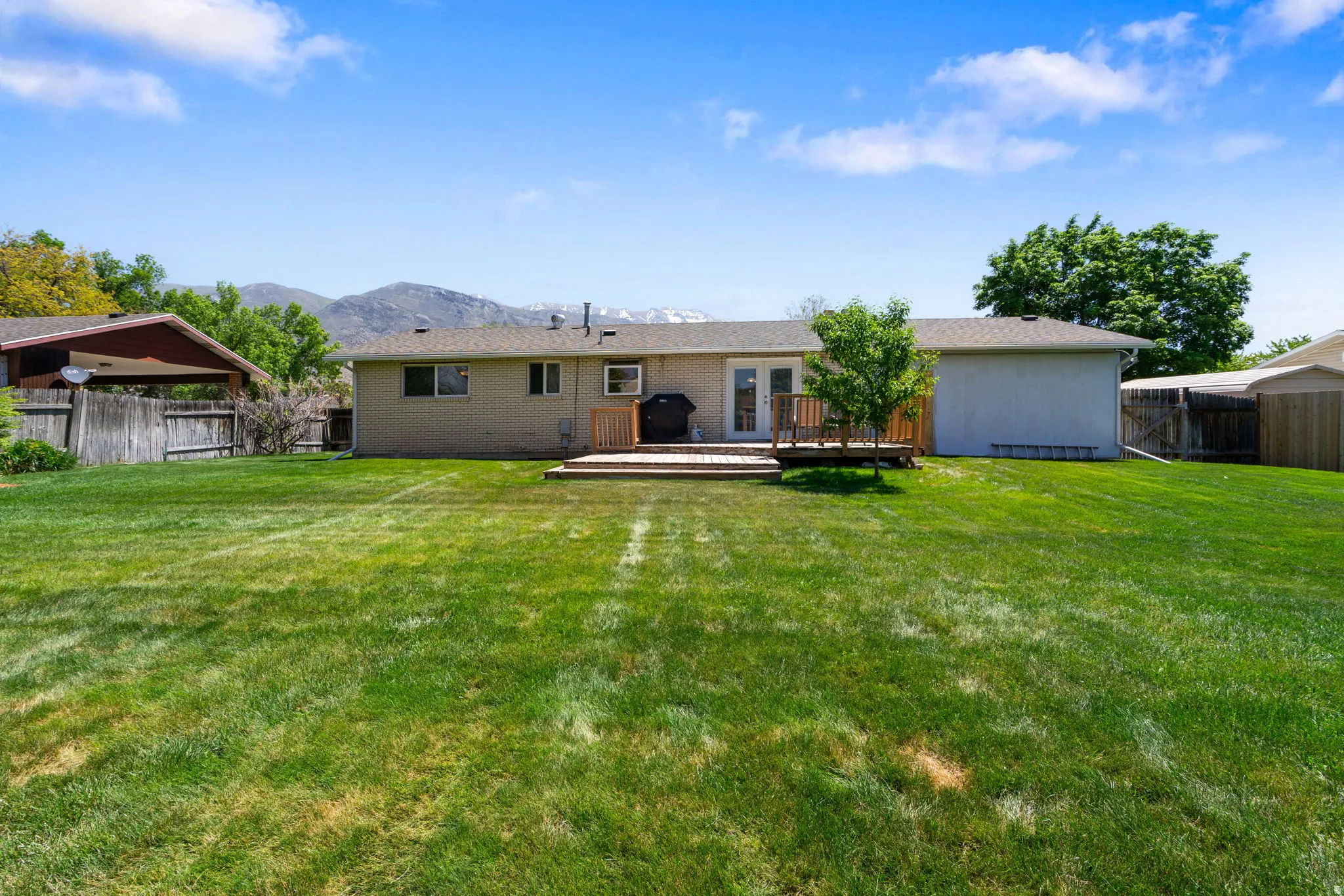 Expansive green lawn with a wooden deck and mountain backdrop