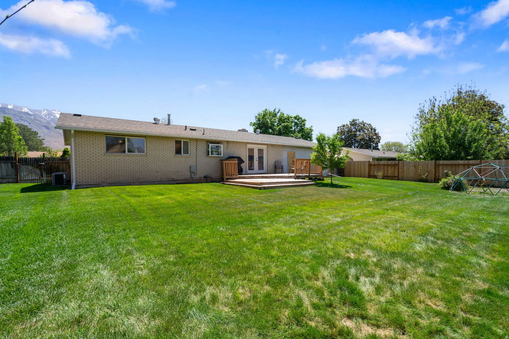 Expansive backyard featuring a large grass lawn, a wood deck, a wood privacy fence, and mature trees