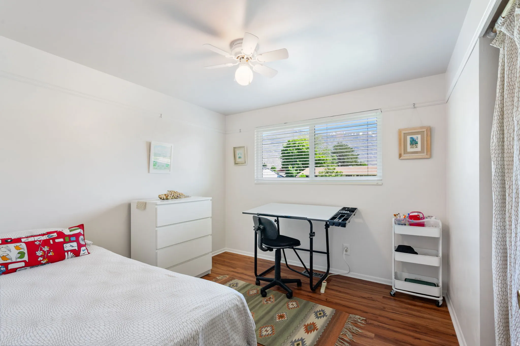 Bright interior space featuring wood-finish flooring, a ceiling fan with integrated lighting, and a window with blinds