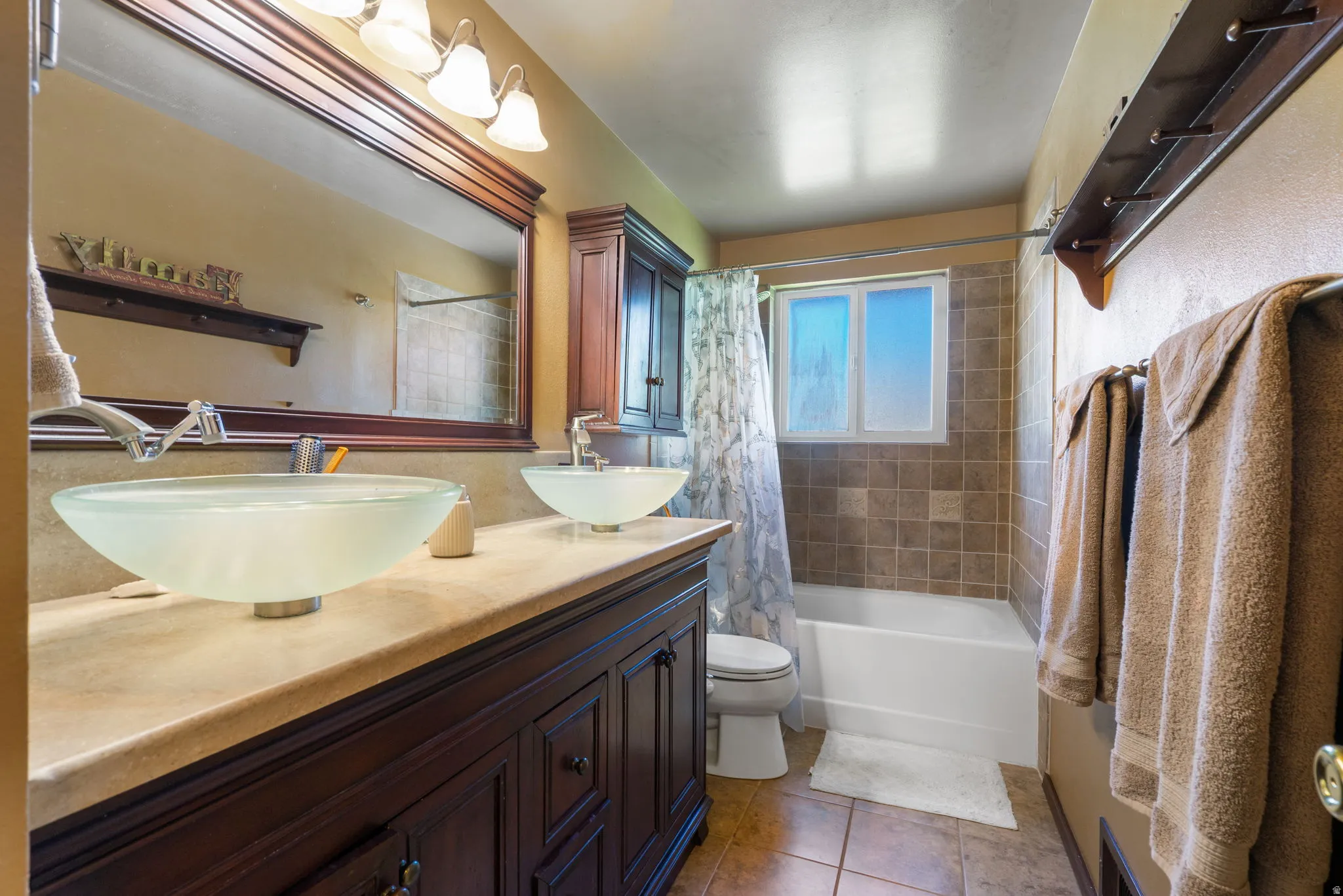 Dual vessel sinks with modern faucets, set into a spacious vanity with dark wood-finish cabinetry and a light-toned countertop