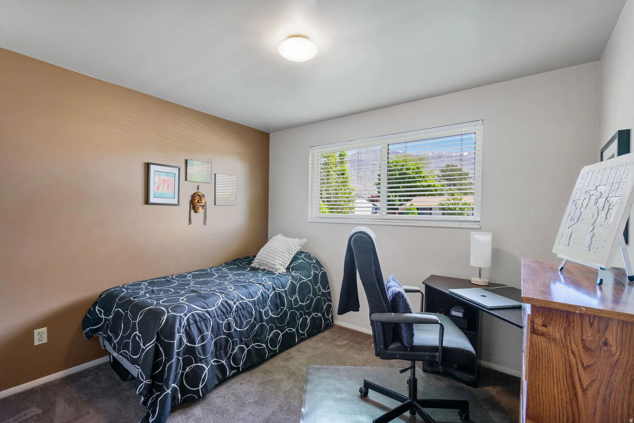 Carpeted room featuring a single window with horizontal blinds, a brown accent wall, a flush-mount ceiling light fixture, and light-colored walls