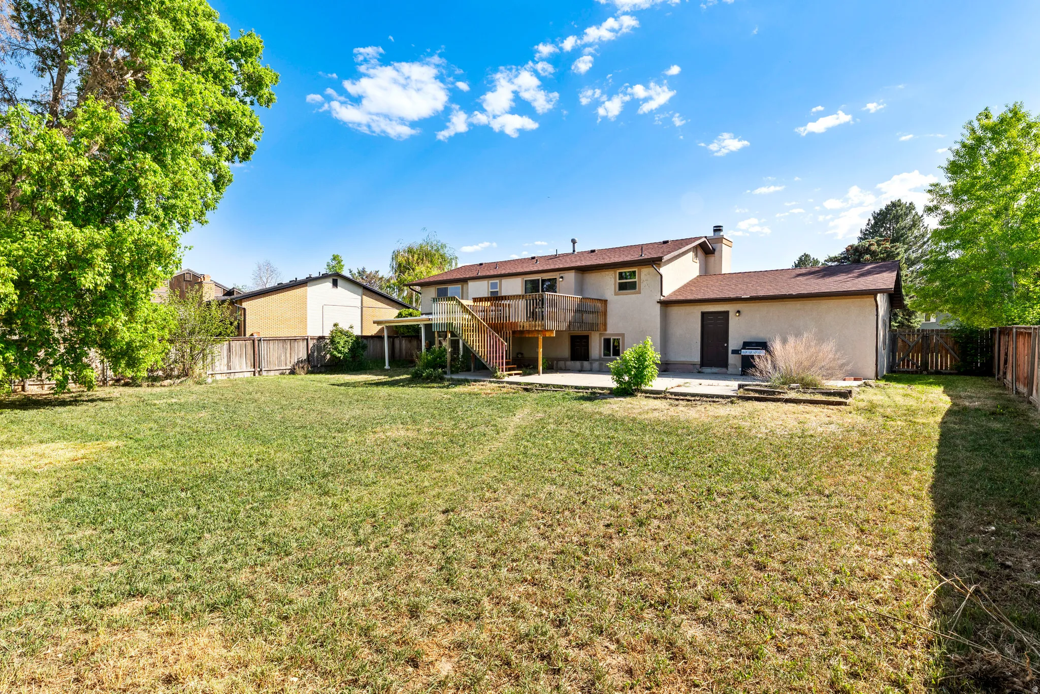 Expansive backyard featuring a large grass area, mature perimeter trees, and a wood privacy fence