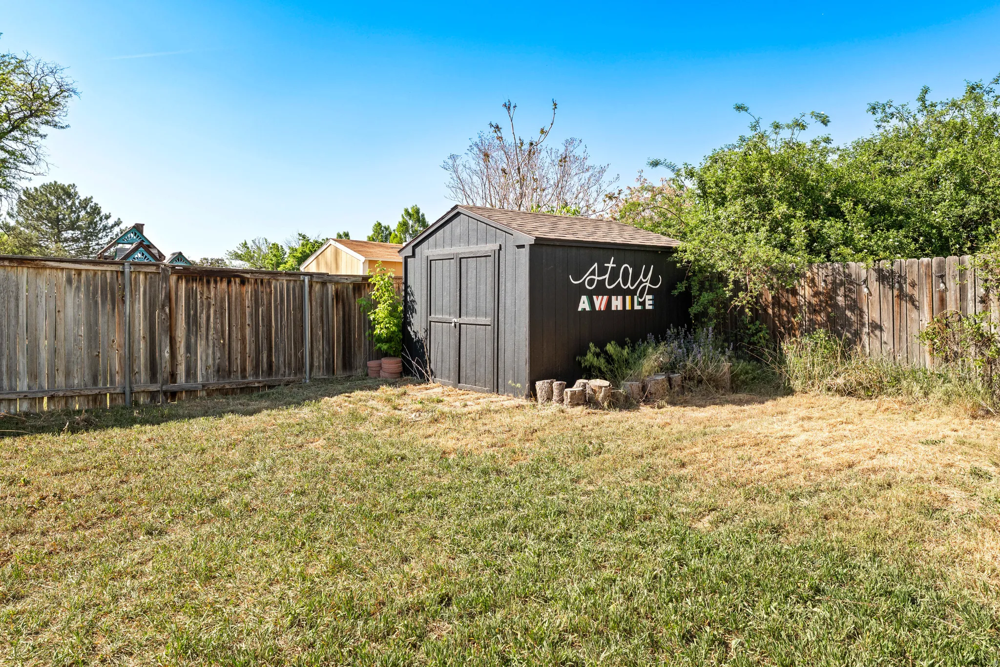 Rear yard featuring a dark-toned storage shed with a shingle roof, surrounded by mature perimeter fencing