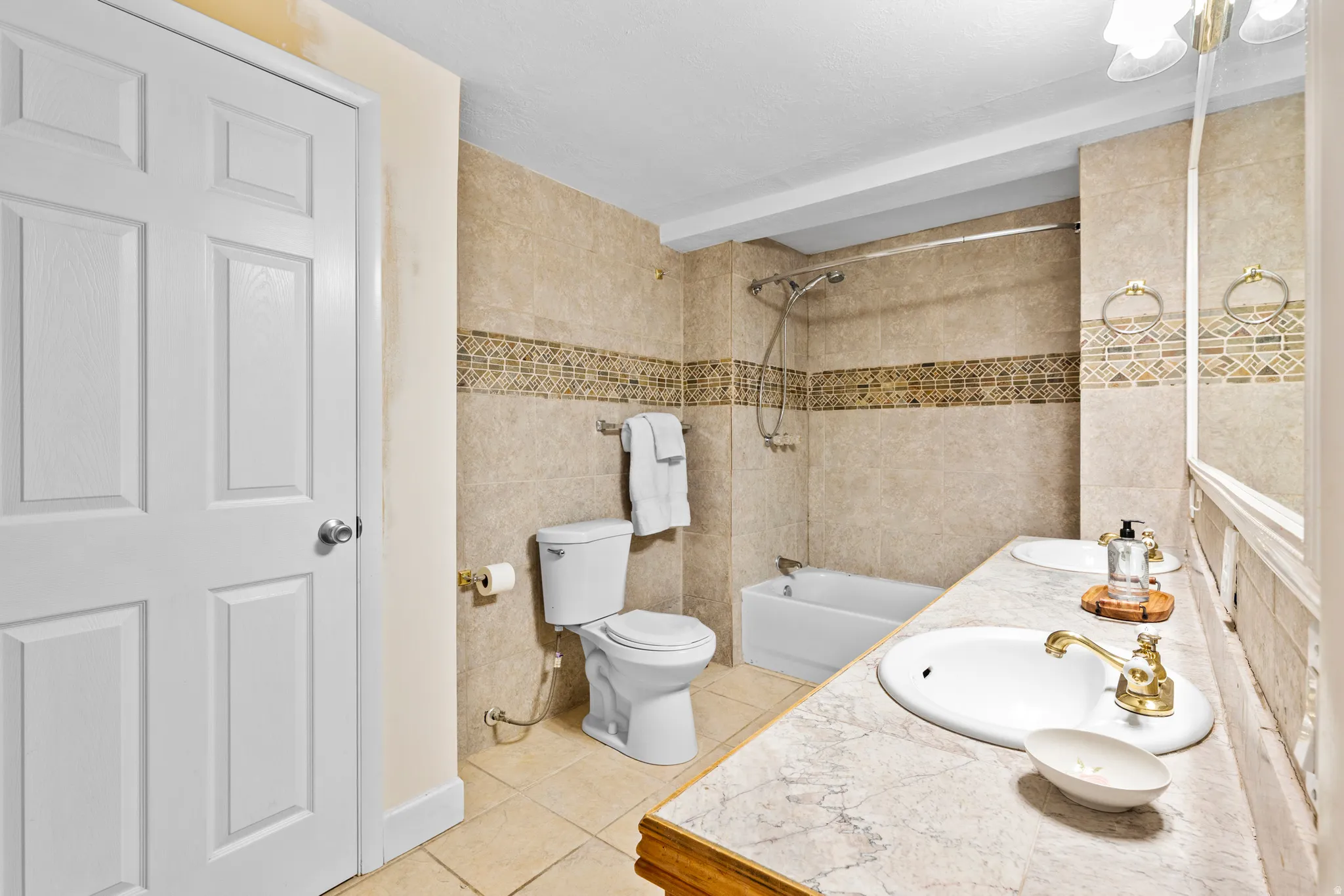 Bathroom featuring a dual vanity with undermount sinks, a bathtub with a shower, and full height wall tiling