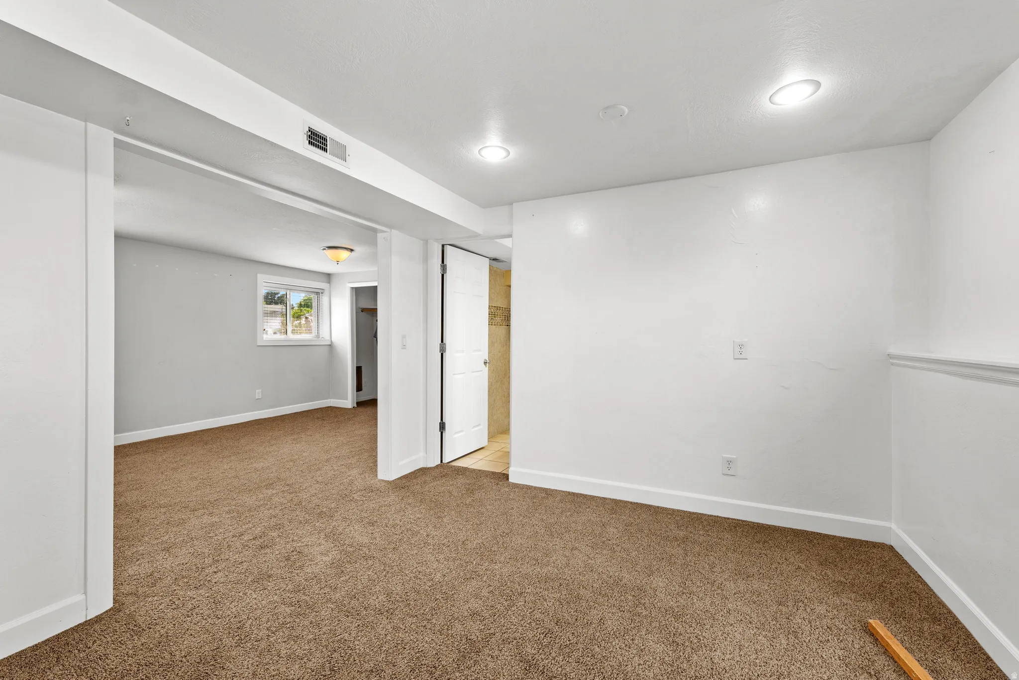 Carpeted interior space featuring white walls, recessed lighting, and a doorway opening to an additional room with a window