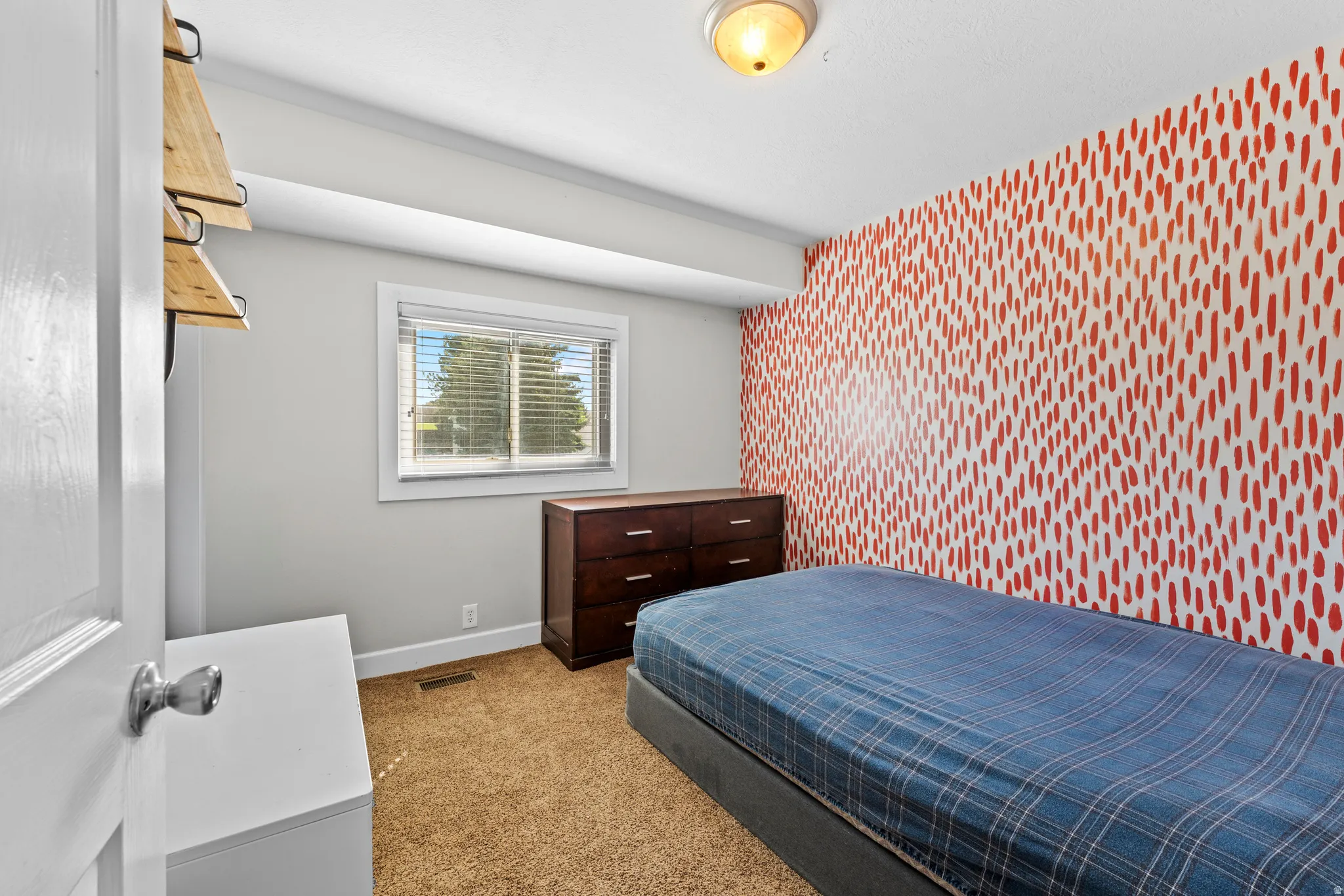 Bedroom featuring a decorative accent wall, carpet flooring, and a large window with blinds