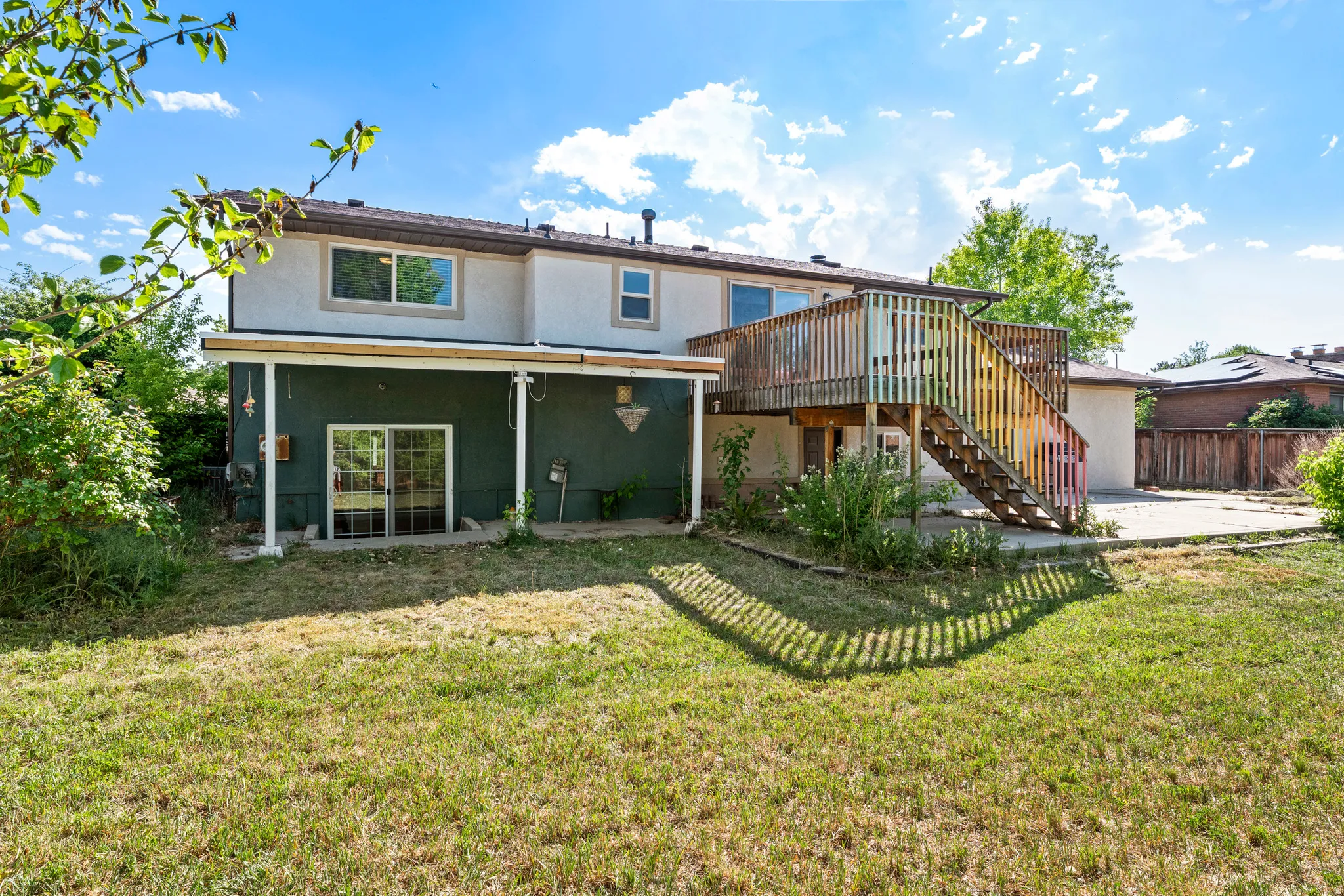 Rear exterior featuring a raised wooden deck with staircase, ground-level covered patio, and dual-pane sliding glass doors
