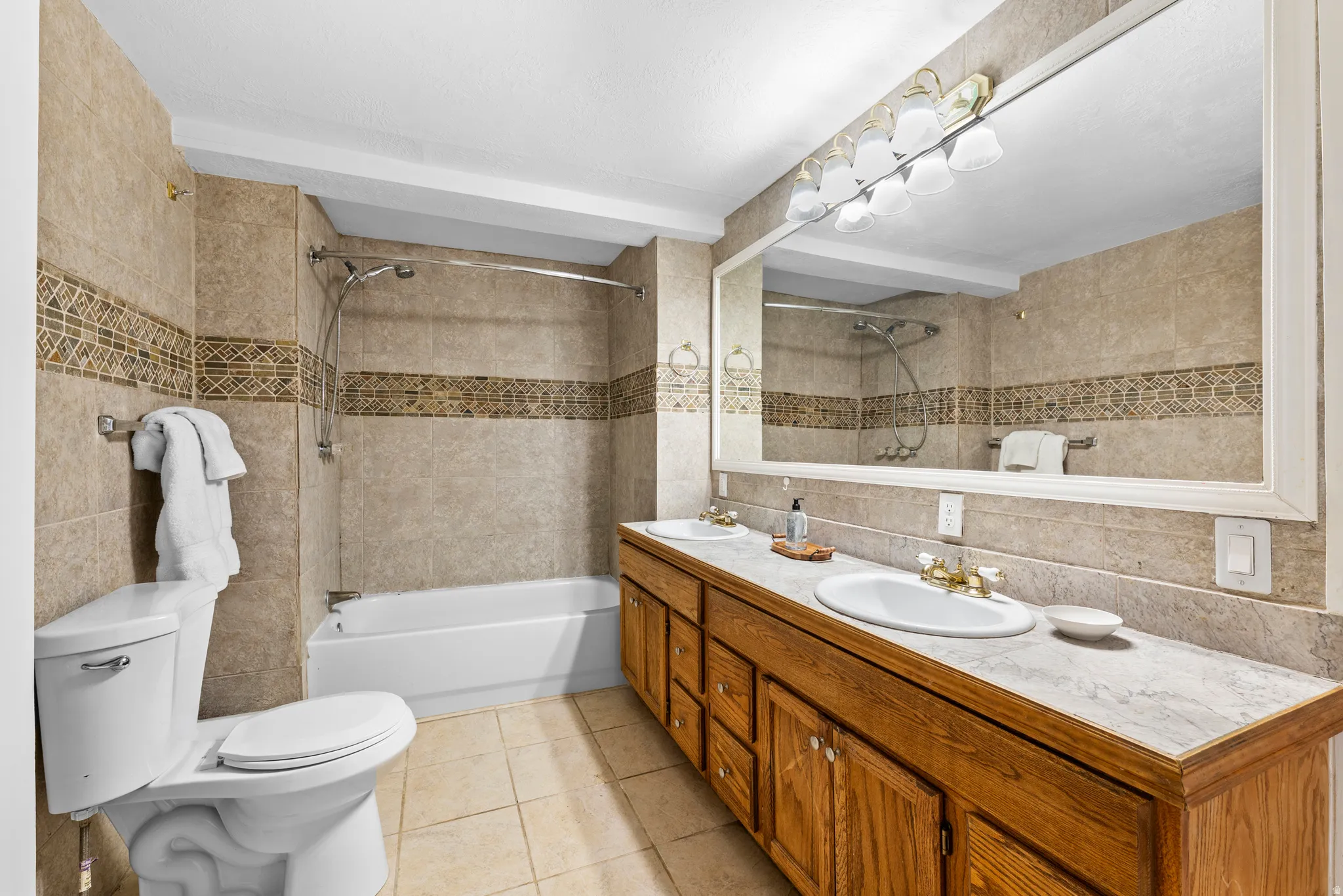 Bathroom featuring a spacious double vanity with wood cabinetry, a large wall-mounted mirror, and a coordinated tile shower surround with decorative accent banding