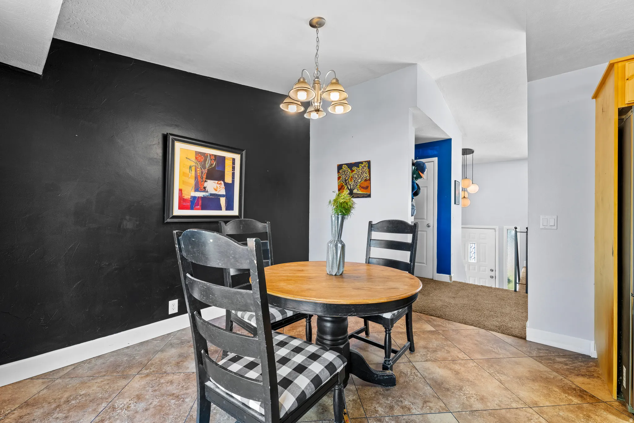 Dining area featuring tile flooring, a contemporary chandelier, and a distinctive accent wall