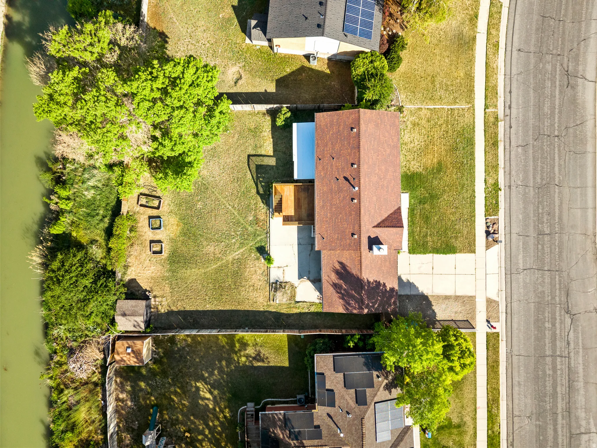 Overhead property view featuring a brown shingle roof, a backyard with mature trees, and a concrete patio