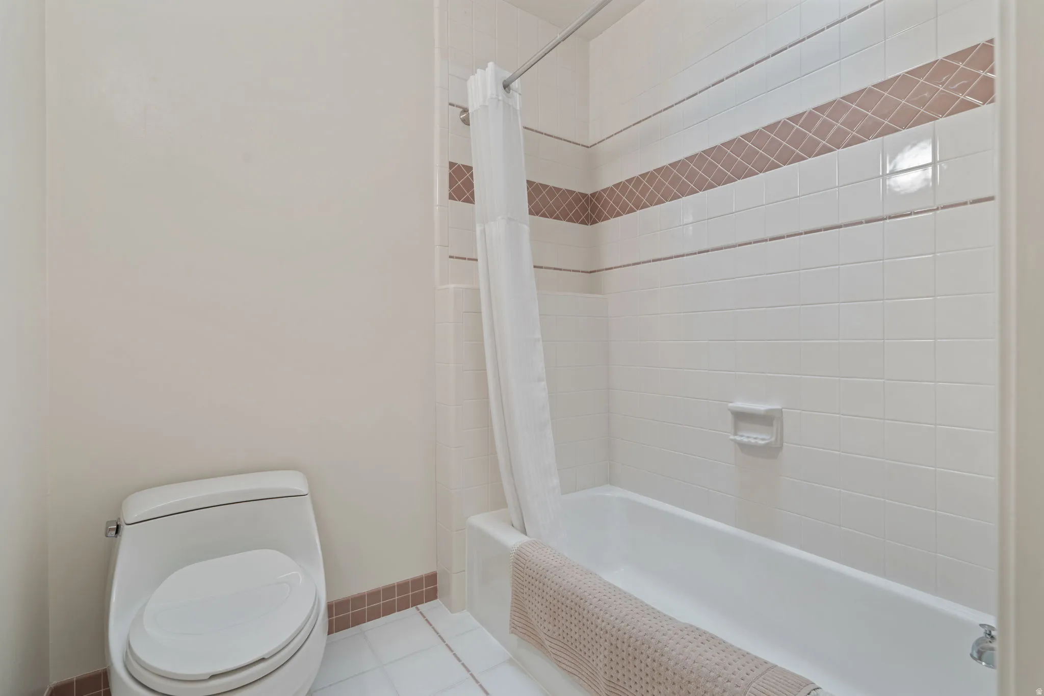 Full bathroom featuring a white tile shower surround with a decorative accent band, a white bathtub, and a modern white toilet