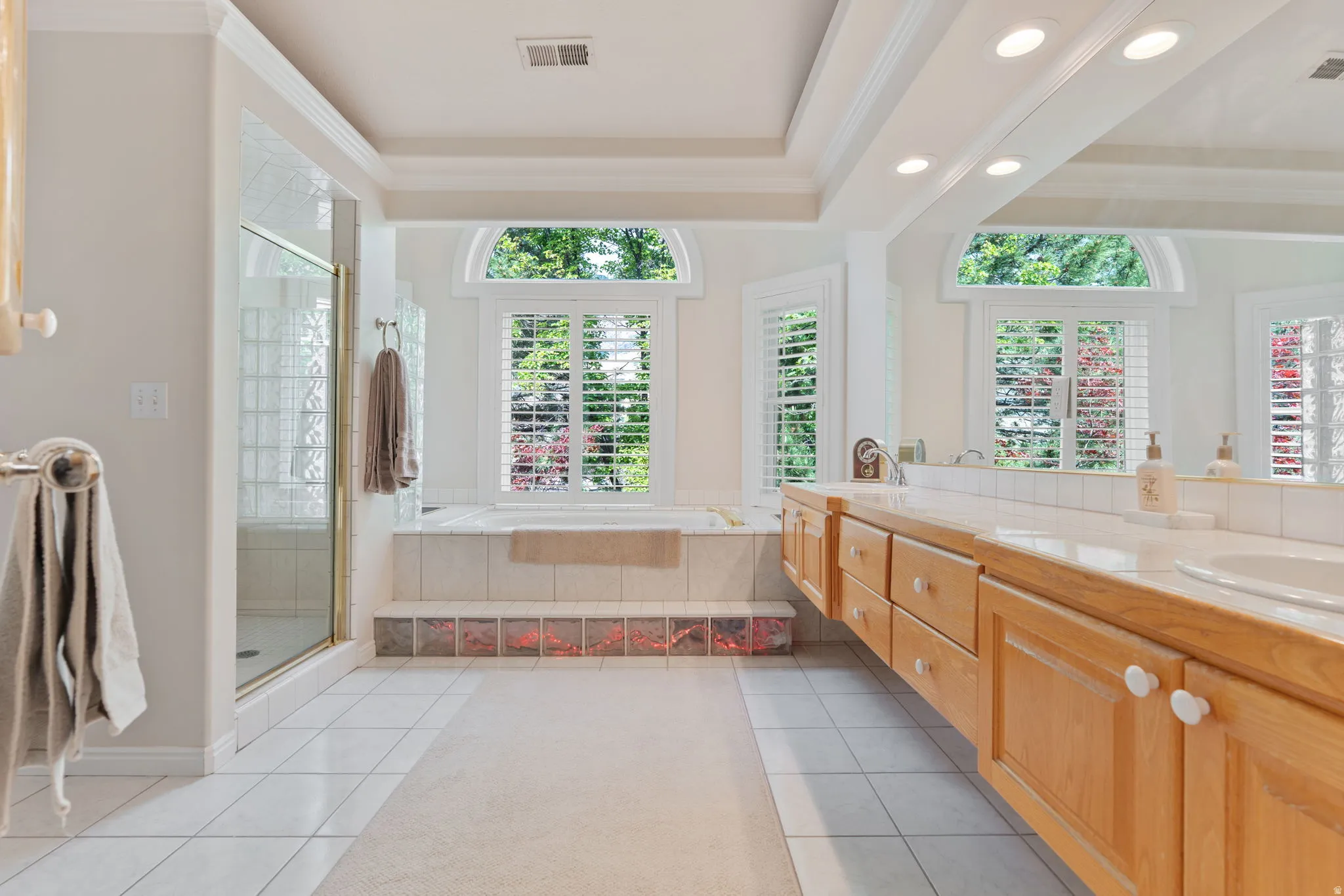 Spacious master bathroom featuring a built-in jetted tub, a separate glass-enclosed shower with glass block detailing, and an extensive vanity with two sinks