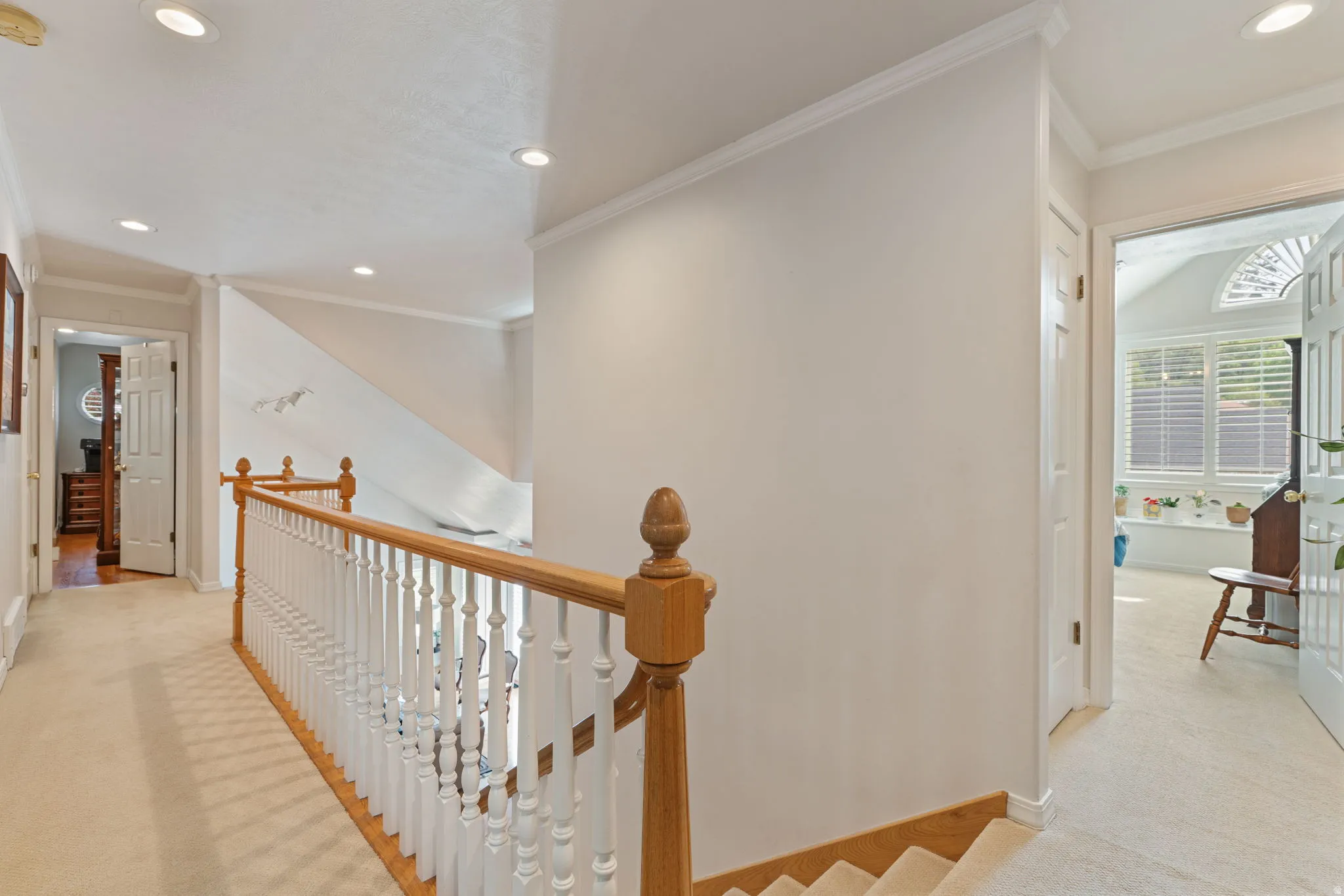 Upper-level landing featuring light-toned carpeting, crown molding, recessed lighting, and a wood-finish handrail with white balusters
