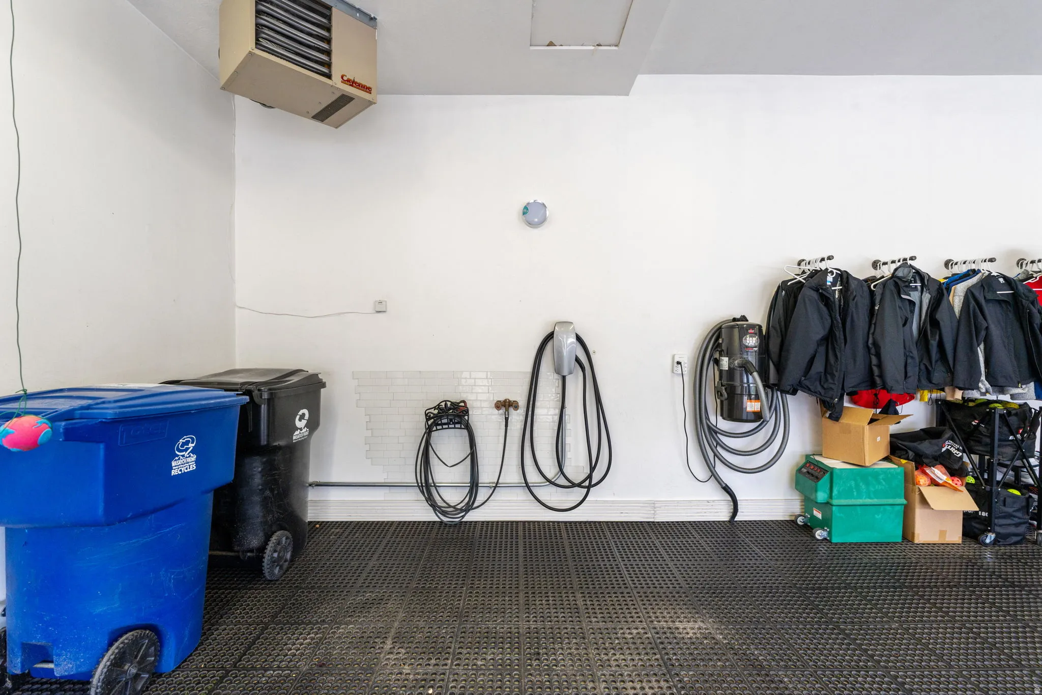 Expansive wall mounted heated garage space with epoxy floors covered with rubber tiles, EV charging station and wall vacuum