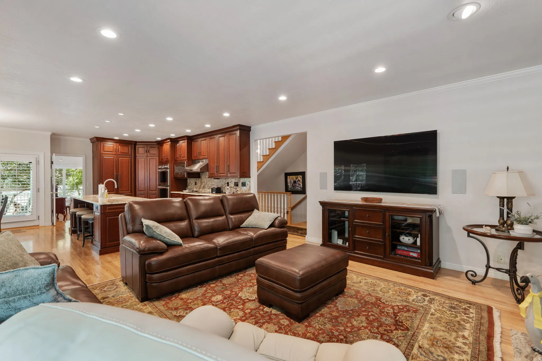 Open-concept living space featuring wood-finish flooring, recessed lighting, a kitchen with rich wood cabinetry, a central island with bar seating, and a stainless steel range hood