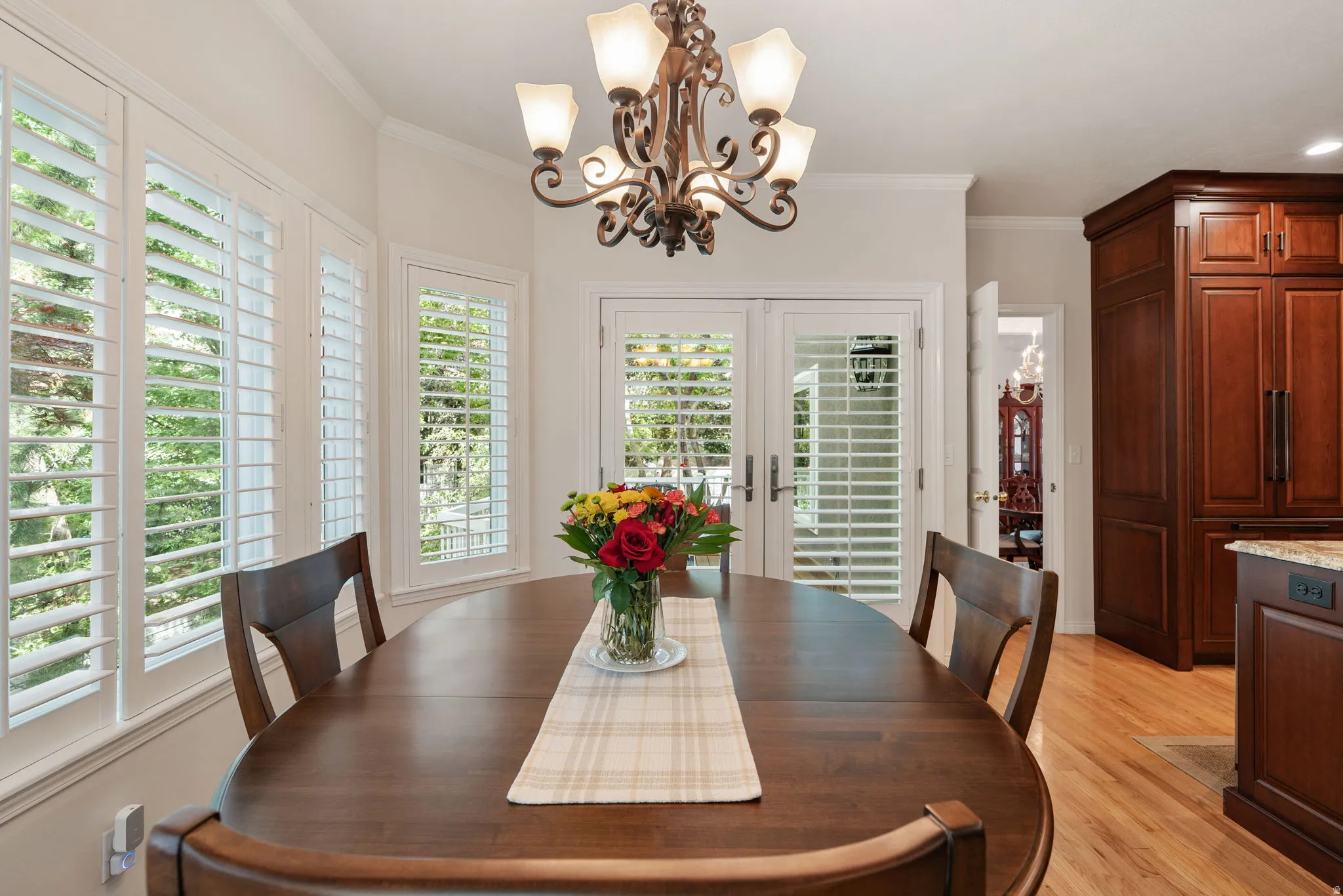 Breakfast area featuring hardwood flooring, white crown molding, a decorative chandelier, and white plantation shutters on multiple windows and French doors