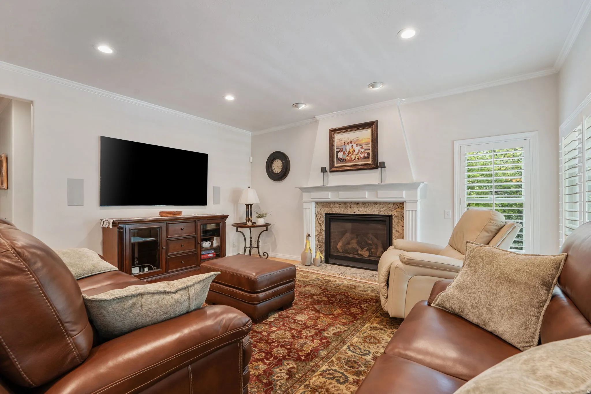 Family room featuring a gas fireplace with temperature control remote, a stone surround and white mantel, recessed lighting, crown molding, and plantation shutters on the windows, and surround sound