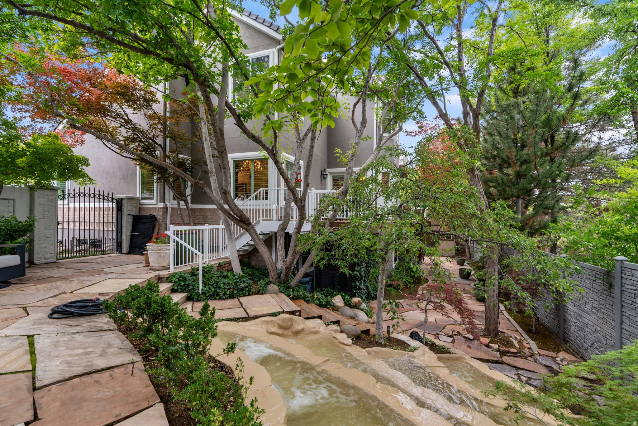 Mason cut stone patio featuring a flowing water feature,, established trees, and a private side iron gate
