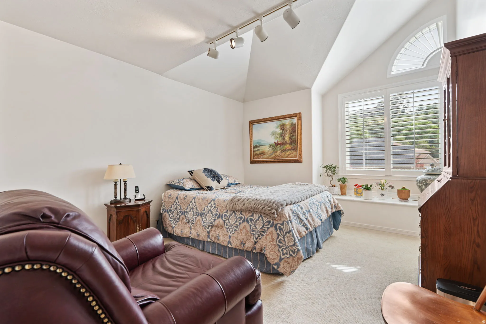 Vaulted ceiling with track lighting, prominent window featuring plantation shutters, an arched transom window, and a built-in window seat