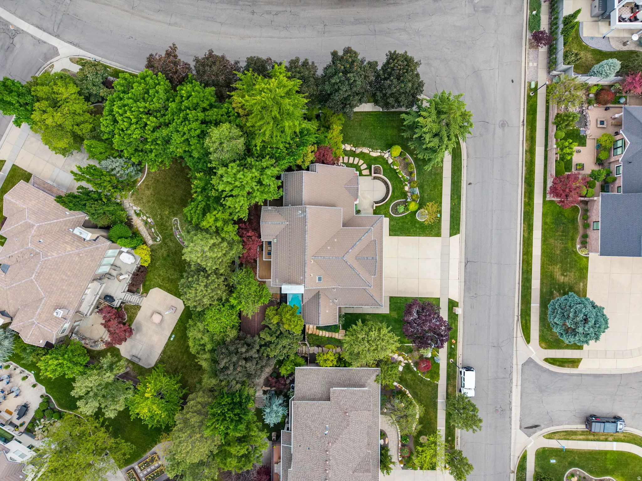 Residential property on a corner lot featuring extensive landscaping, a paved driveway, and mature trees