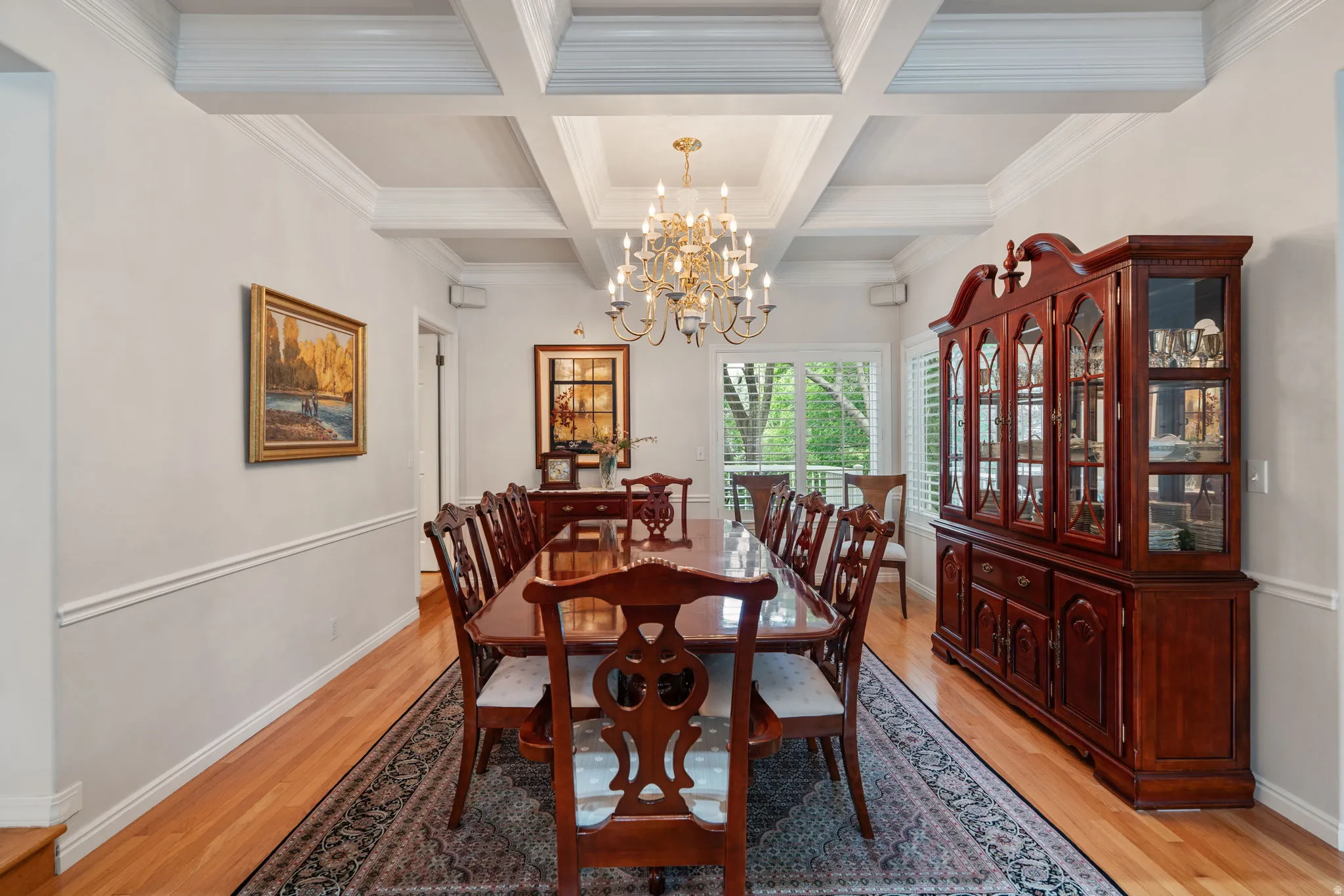 Dining area featuring a coffered ceiling, a brass chandelier, wood-finish flooring, and white plantation shutters