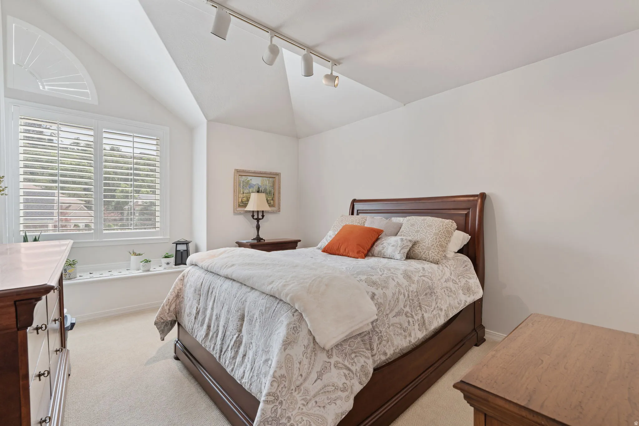 Vaulted ceiling room featuring a large window with plantation shutters, an arched transom window, and track lighting