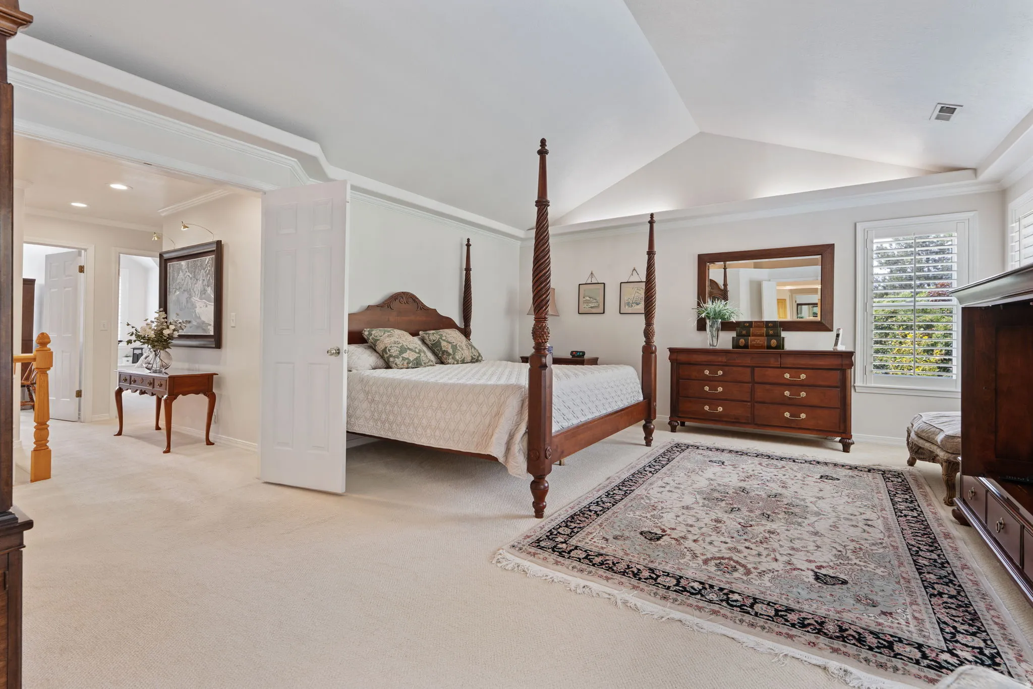 Expansive bedroom featuring vaulted ceilings, light-colored carpeting, and plantation shutters
