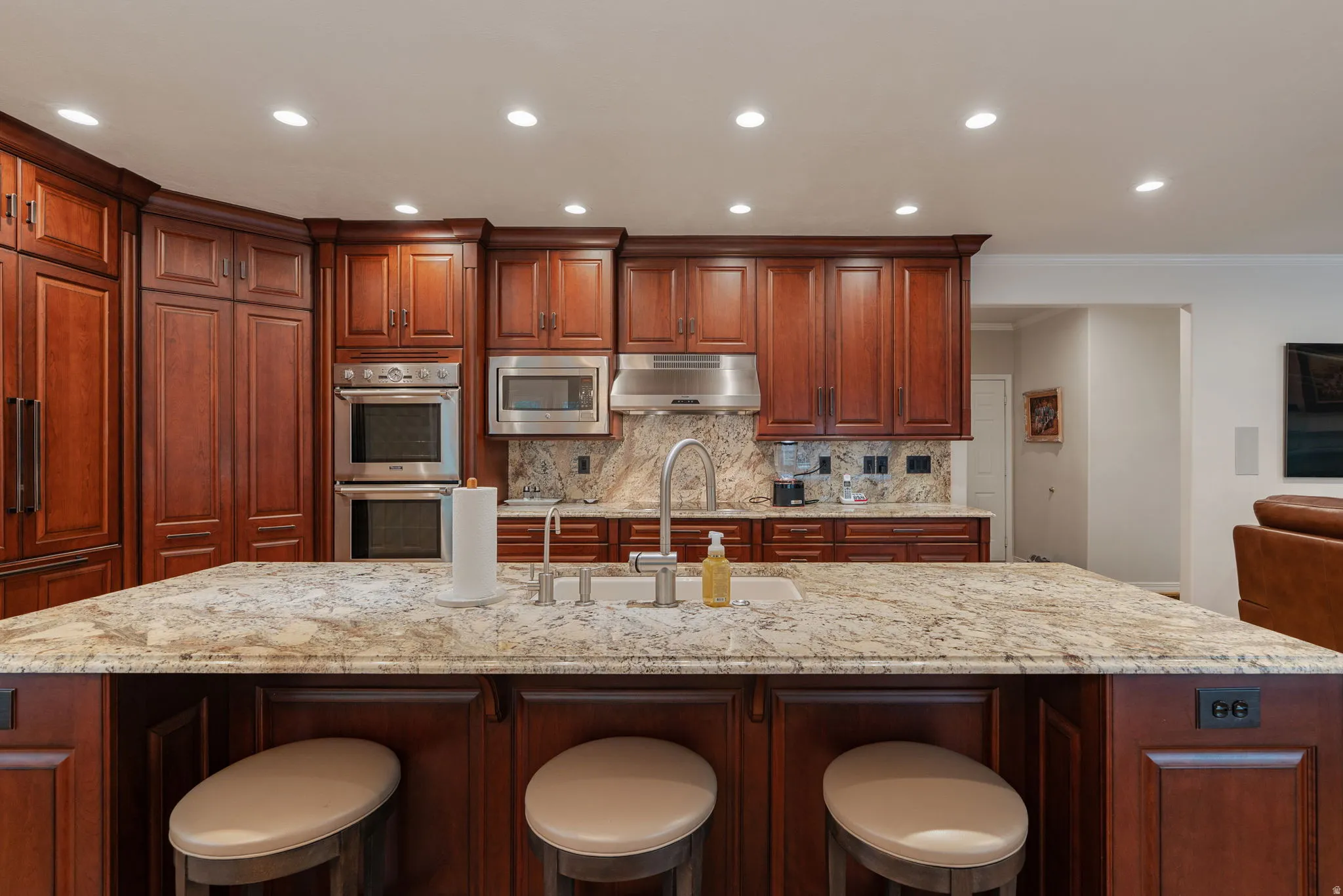 Kitchen featuring a large island with granite countertop, mahogany wood cabinetry, stainless steel Thermador double ovens, stainless steel microwave, and integrated refrigerator and dishwasher