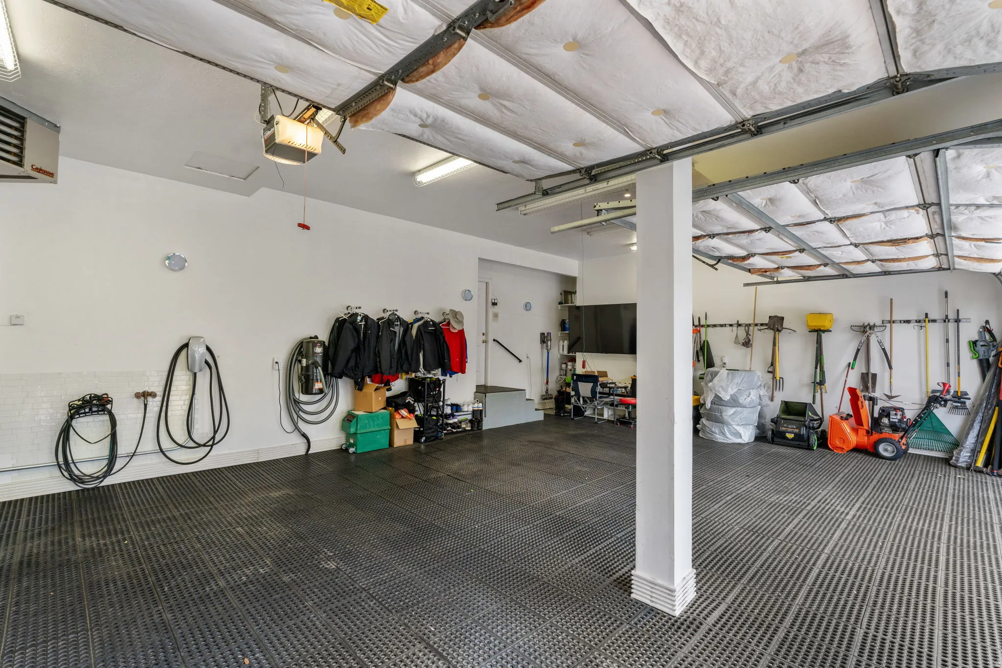 Expansive heated garage space with epoxy floors covered with rubber tiles, EV charging station and wall vacuum