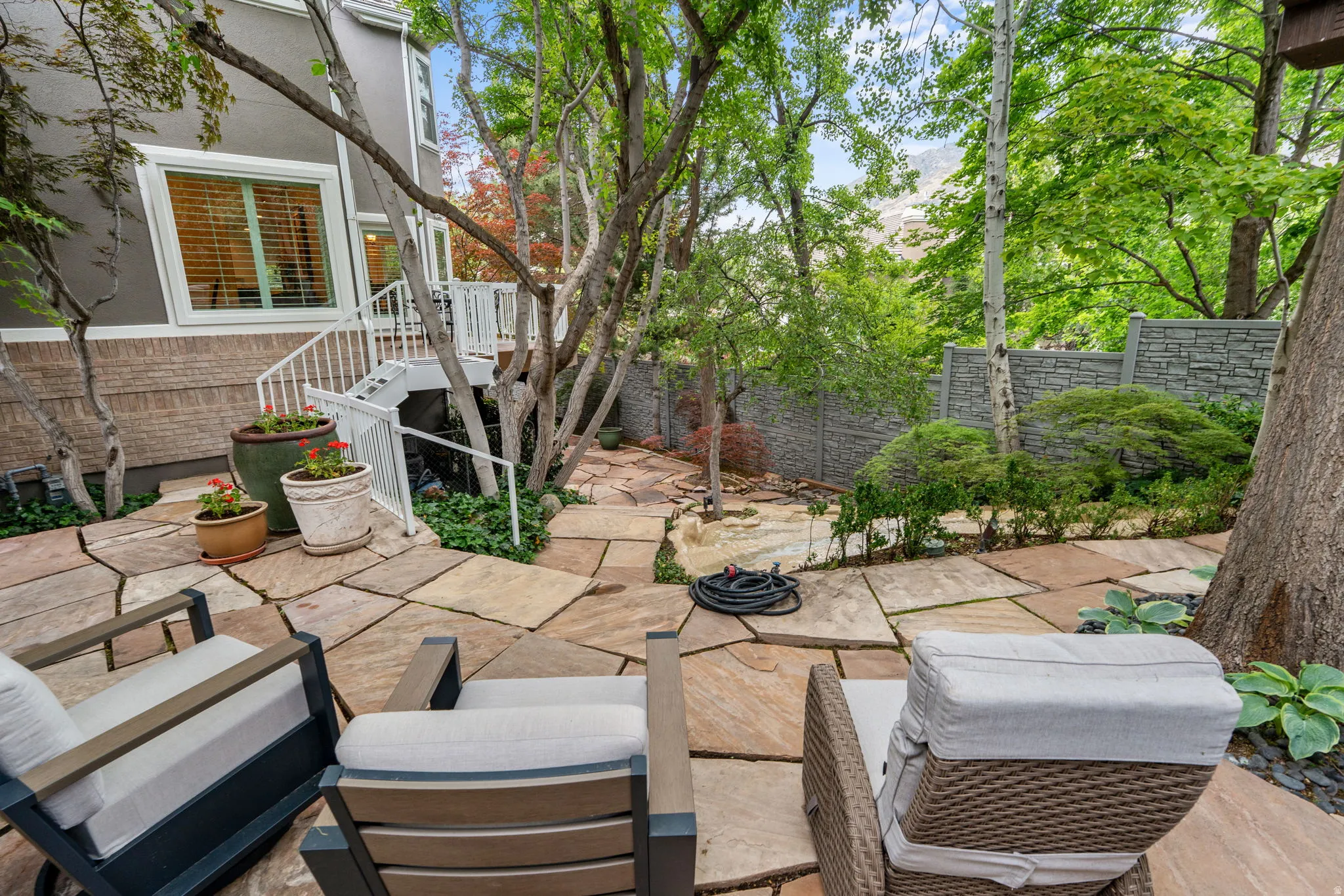 Custom cut stone patio featuring mature trees, a stone retaining wall, and a staircase leading to an upper level