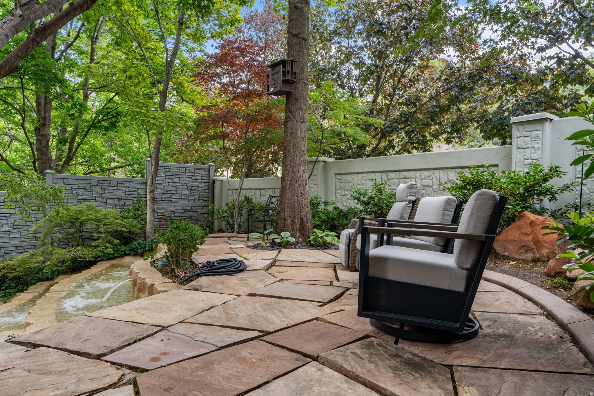 Outdoor patio featuring custom cut stone patio, a stone water feature, and a textured privacy wall