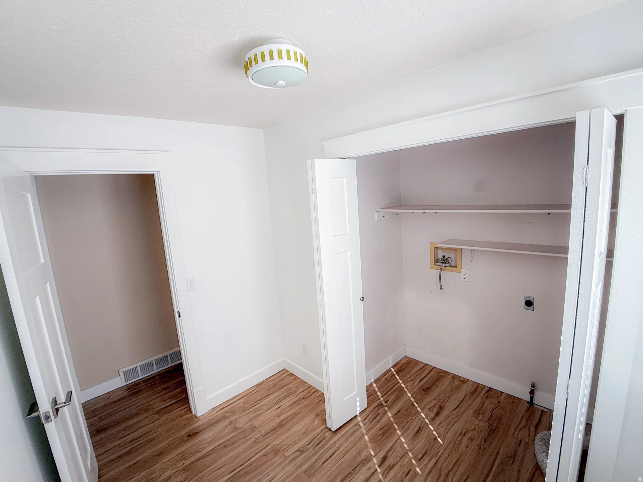 Utility space featuring wood-finish flooring, white walls, and a modern ceiling light fixture
