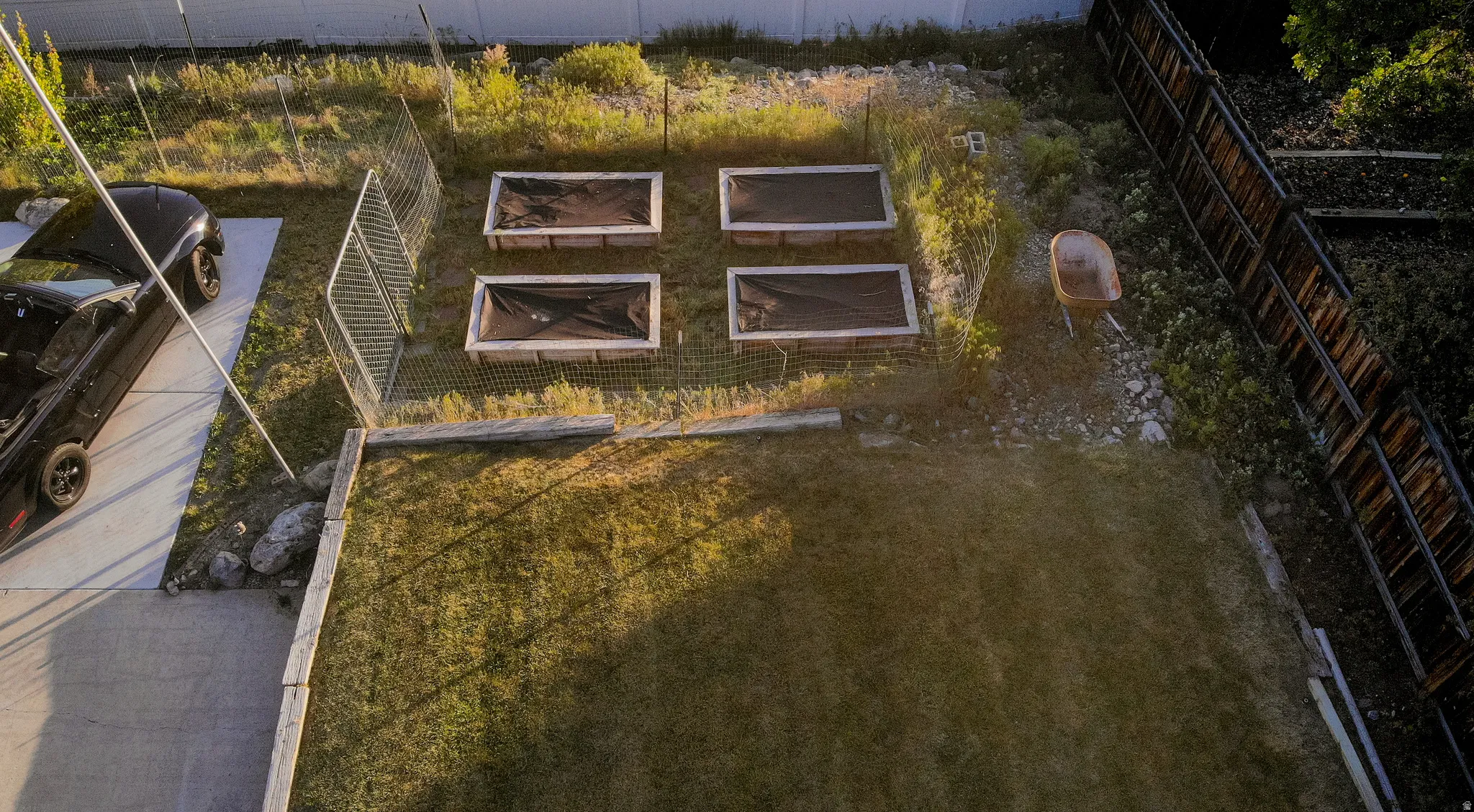 Backyard featuring four raised garden beds with protective coverings, a concrete driveway, a chain-link fence, and a wooden privacy fence