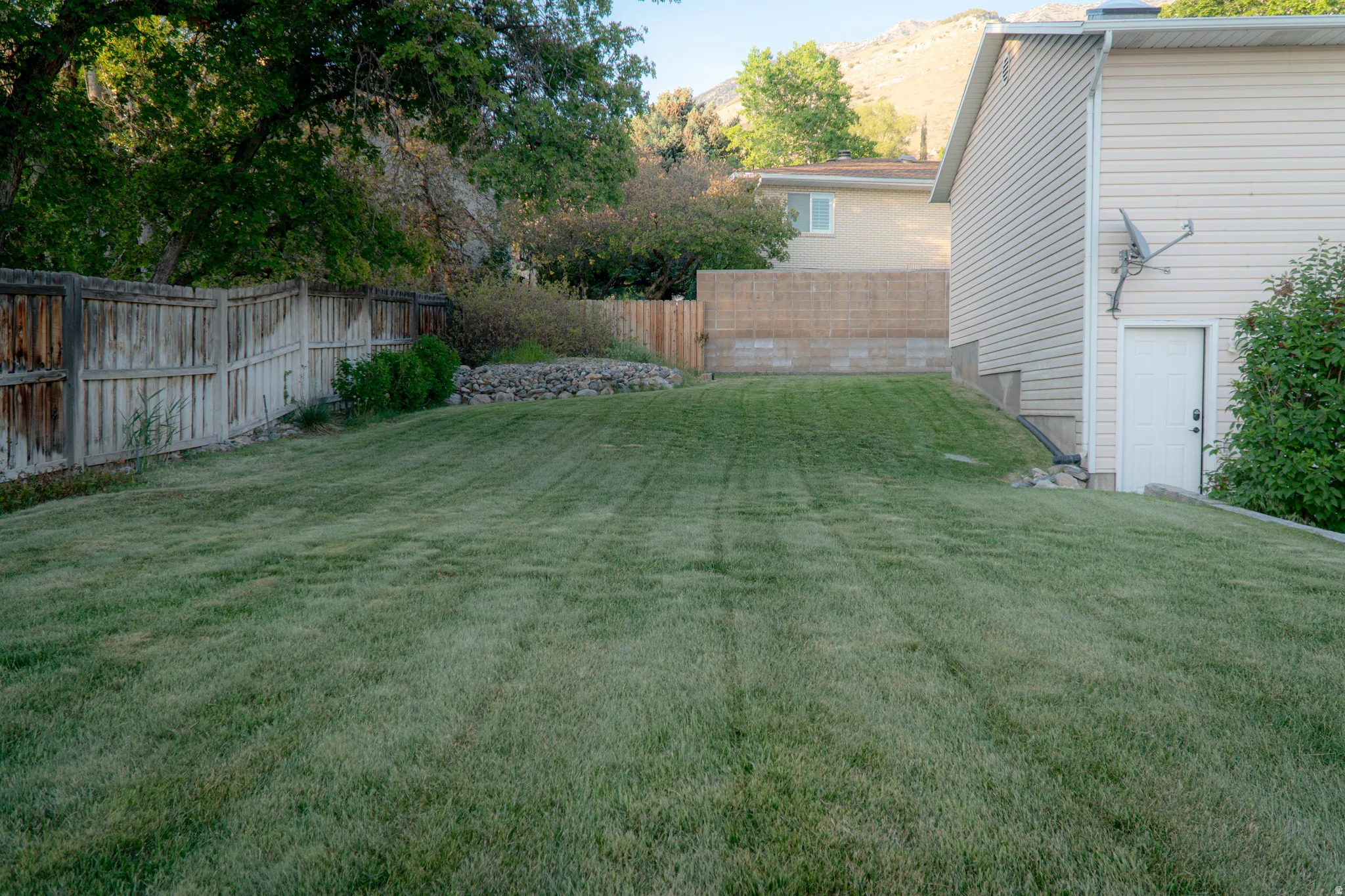 Expansive green lawn with mature trees and a wood privacy fence