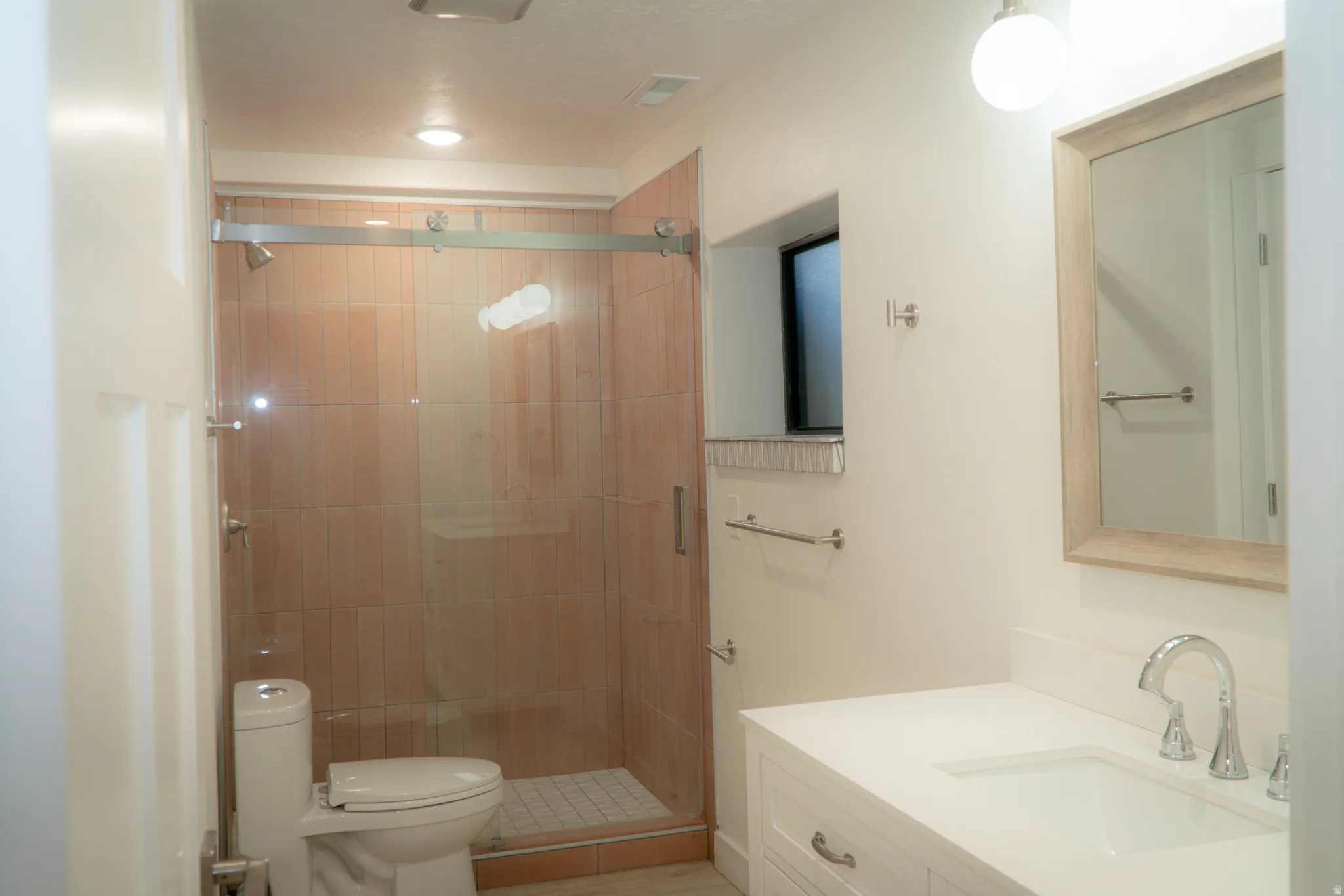 Contemporary bathroom featuring a spacious glass-enclosed shower with tile surround, a white vanity with integrated sink, chrome fixtures, and a framed mirror
