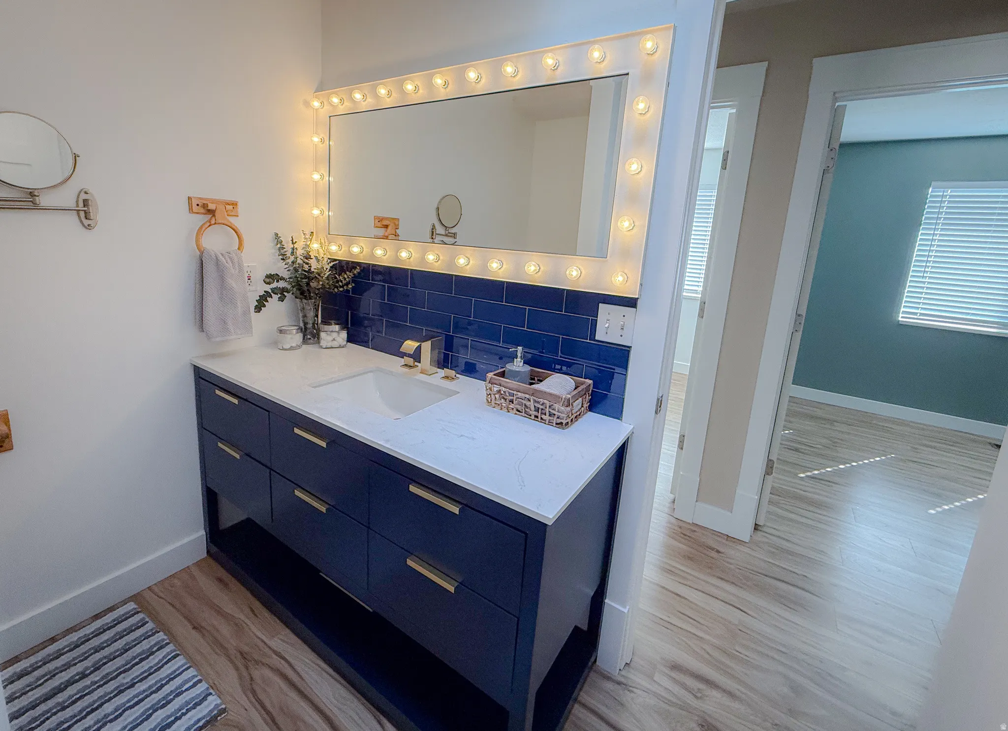 Vanity area featuring a navy blue cabinet with gold-finish hardware, a white countertop with an integrated sink, a tiled backsplash, and wood-finish flooring