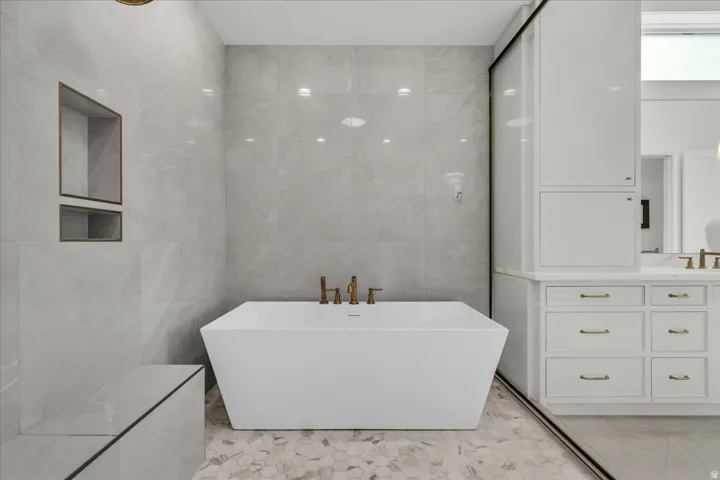 Primary bathroom: freestanding soaking tub with brass fixtures, set against large format wall tiling and hexagonal floor tiling
