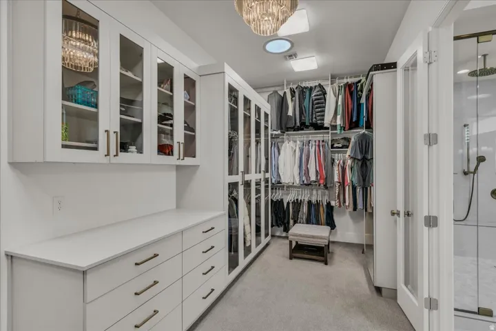 Spacious primary closet featuring custom cabinetry, integrated shelving, and glass-front upper storage