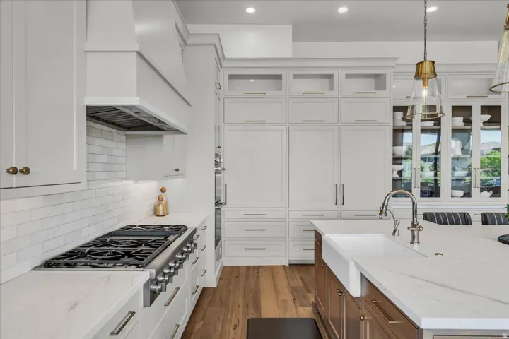 Gourmet kitchen featuring a professional-grade gas range, custom range hood, white subway tile backsplash, integrated paneled appliances, and an oversized island with a farmhouse sink