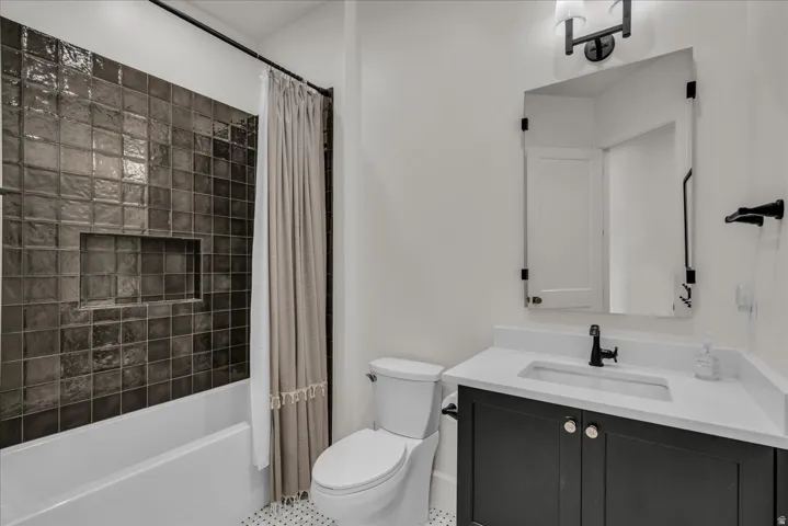 Bathroom featuring a dark tiled tub/shower combination with an integrated niche, a white vanity with an undermount sink and matte black faucet, a framed mirror, and hexagonal floor tiling