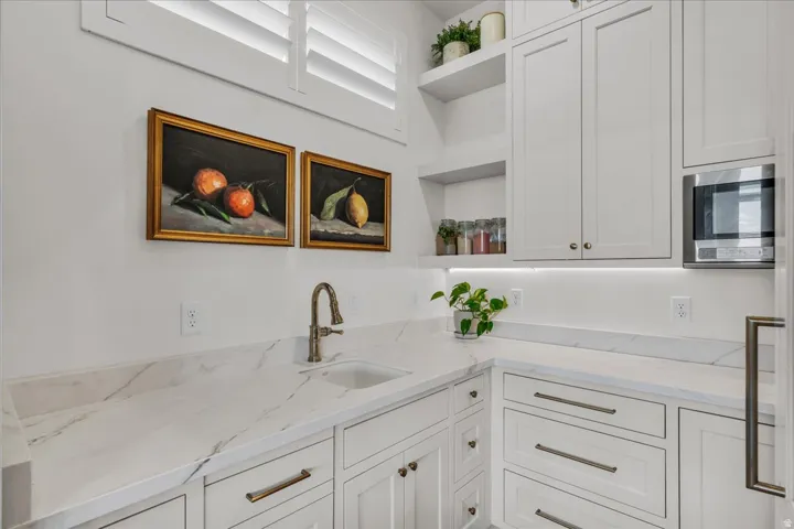 White shaker cabinetry with brass hardware, marble-look countertops, and an undermount sink with a bronze-finish faucet