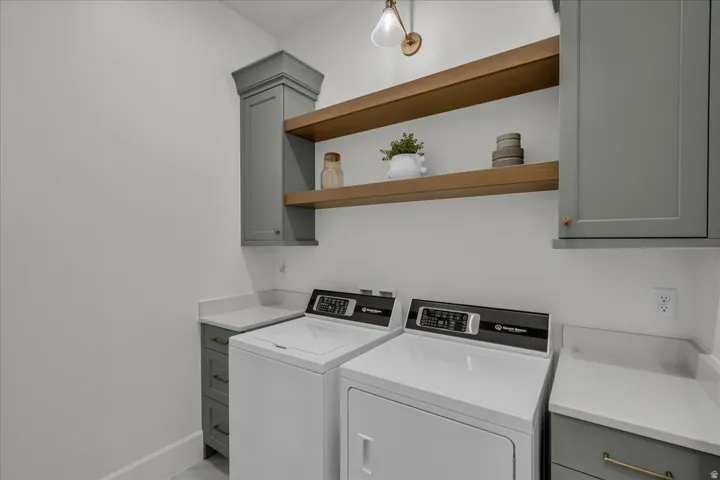 Laundry area featuring light gray cabinetry, wood-finish open shelving, and white countertops