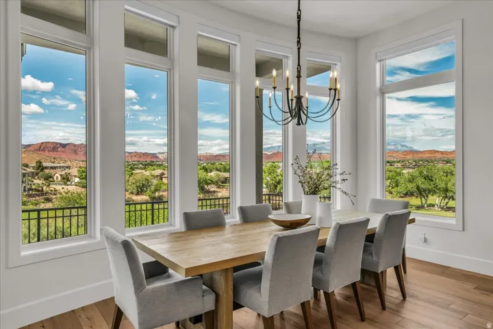 Dining area featuring abundant natural light from multiple tall windows, a wrought iron chandelier, hardwood flooring, and distant mountain scenery