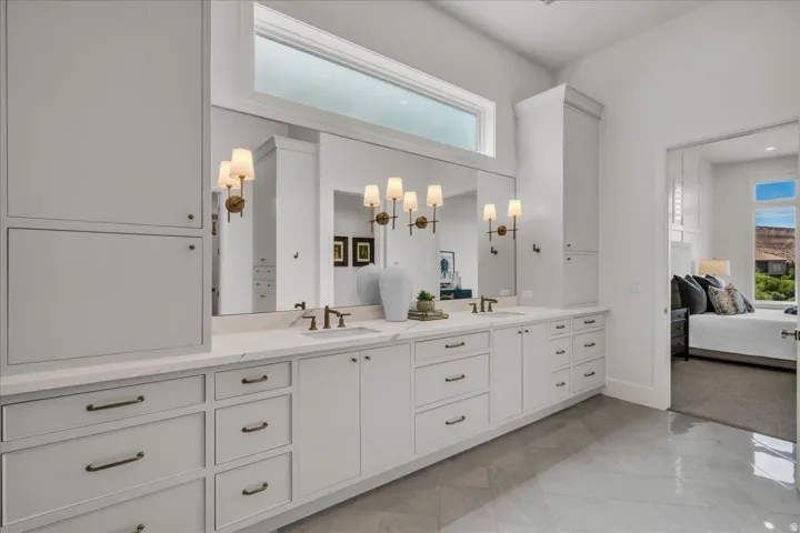 Primary bathroom: dual vanity with integrated sinks, expansive mirror, and sconce lighting