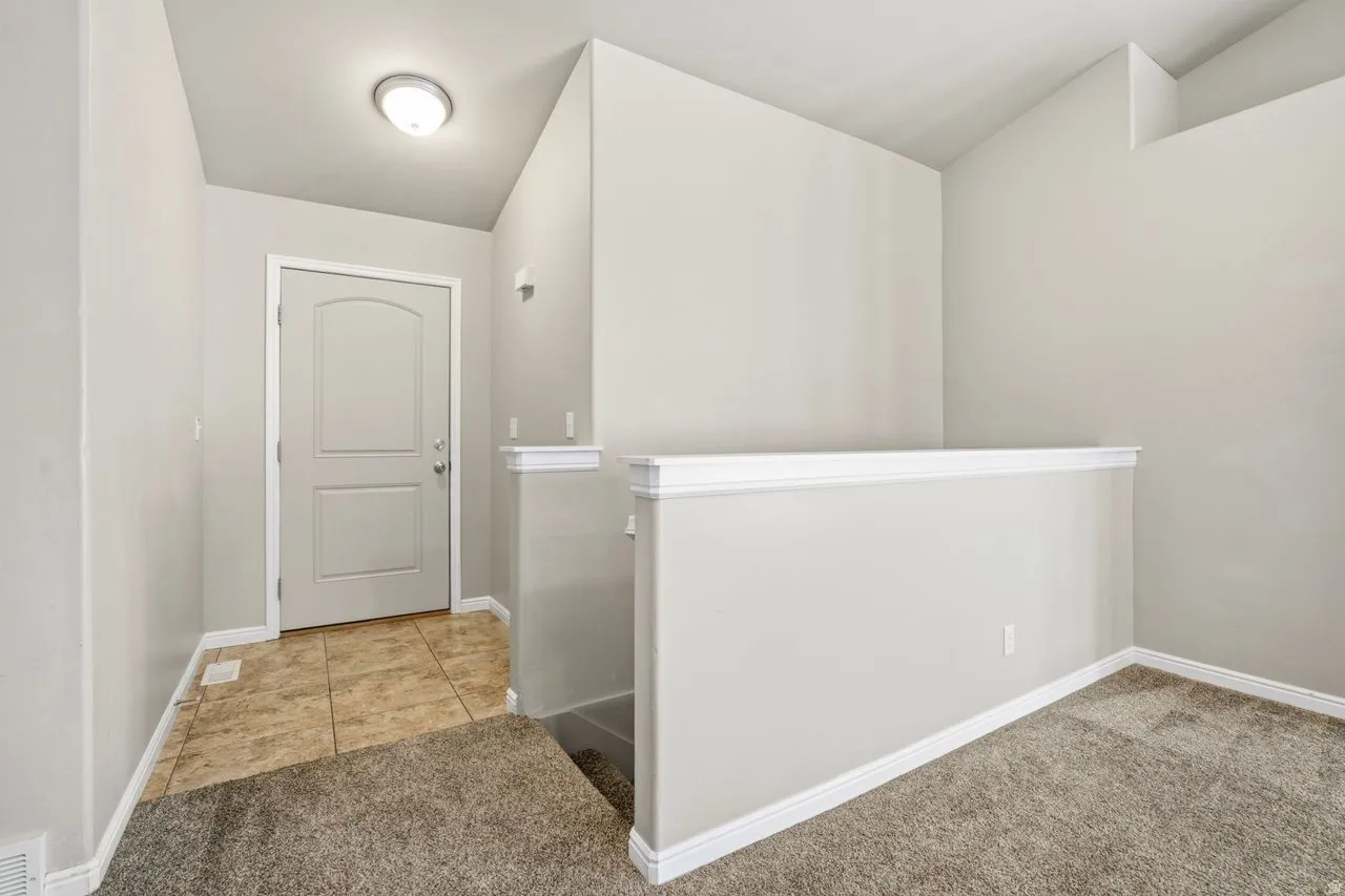 Entryway featuring a two-panel door with an arched top light, overhead flush mount lighting, tiled flooring, and a carpeted landing