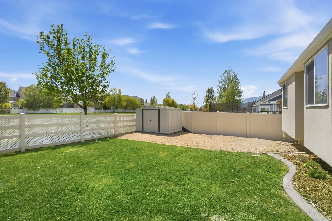 Expansive backyard featuring a lush lawn, white lattice fencing, a detached storage shed, and a dedicated gravel area