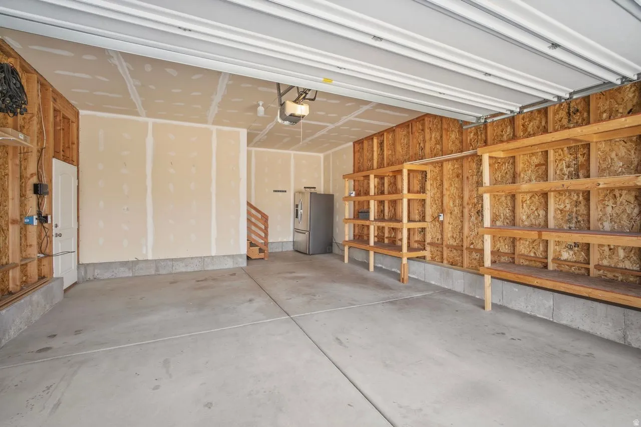 Spacious garage featuring a concrete floor, built-in wooden shelving, exposed framing, a utility door, and a staircase